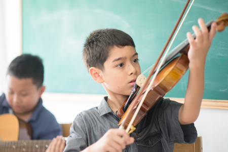 Little boys play and practice violin in the music class roomの写真素材