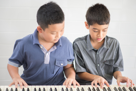 Asian student boys playing piano together in the classの写真素材