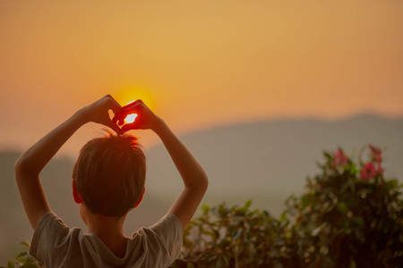 Little boy looking to the sunrise behind the hill in the morningの写真素材