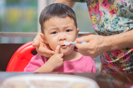 Grandmother feeding meal the baby boy in the houseの写真素材