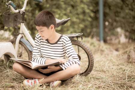 Little boy reading book sitting with bicycle in the parkの写真素材