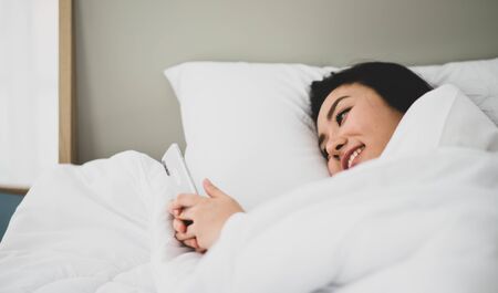 Asian woman type and chat  on mobile phone in the bed