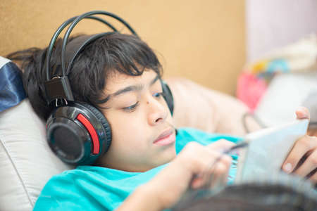 Teen Asian boy with headphone study online, listen music and play gameの写真素材