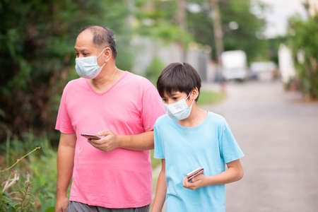 Happy Asian Family Walking In The Park Wearing Medical Face Mask with the phone in handの写真素材