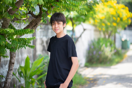 A young Asian boy stands in front of a tree, smiling.の写真素材