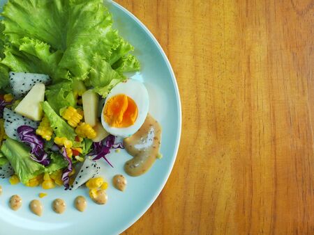 Fruit Salad and Salad Dressing with wooden background, raw material boiled egg, apple, dragon fruit, corn, vegetablesの写真素材