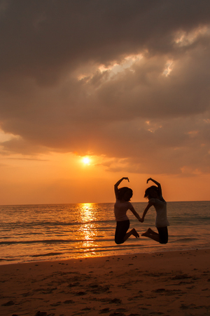 Silhouette photo of love symbol from a couple on the beach at sunsetの写真素材