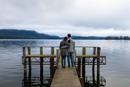 Young Asian couple hugging leaning on shoulder on the bridge Lake Te Anau New Zealandの写真素材