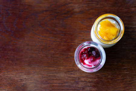 Greek yogurt with berries and mango in glass jars on wooden backgroundの写真素材