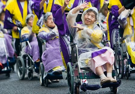 Kagoshima City, Japan, November 3rd, 2008. Elderly Japanese Festival Dancers in wheelchairs at the Ohara Matsuri dance festival. They are being pushed by young volunteers who are also holding umbrellas to ward off the rain. A photo representative of many のeditorial素材