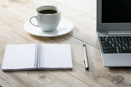 Blank notepad and a pen next to a laptop and coffee on a wooden vintage deskの写真素材