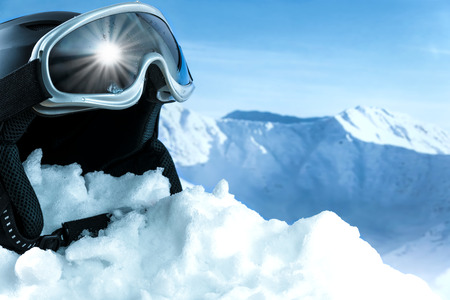 Helmet and ski goggles on snow with a blue sky and mountainsの写真素材