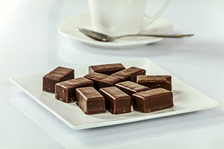 Chocolates on a plate next to a cup of coffee in the officeの写真素材