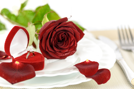Table setting for a romantic dinner  with Gold engagement ring with diamonds in an elegant velvet box and a red rose.の写真素材