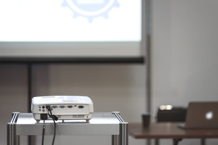 White multimedia projector in a conference room with blured projection screen and a lecturer desk on the background (reduced tone)の写真素材