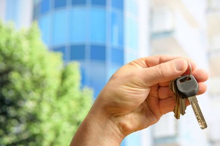 The customer holds the keys to the new apartment against the background of a modern glass building on a sunny dayの写真素材