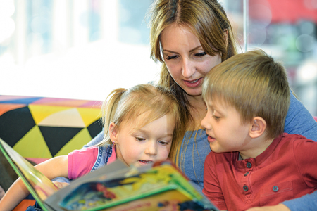 Portrait of pretty young women reading fairy tales with two children in the children's playroomの写真素材