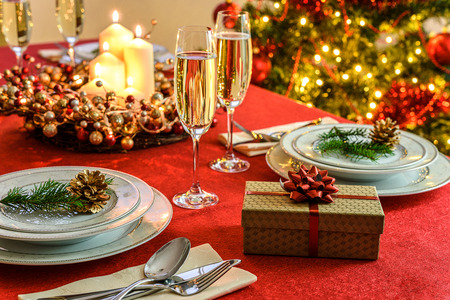 Beautifully decorated Christmas table - gift, glasses of champagne and tableware with Christmas decoration on a red tablecloth.の写真素材