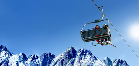 Composite image of skiers on a ski lift in high mountains on the background of a clear blue sky with large copy space.の写真素材
