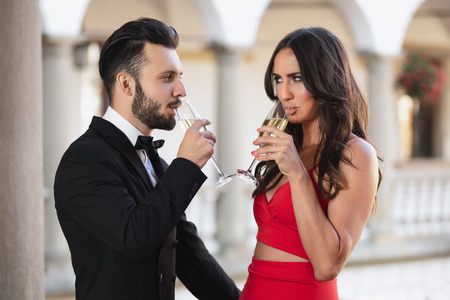Elegant couple of lovers with a glass of wine or champagne standing on a balcony during luxury party.の写真素材