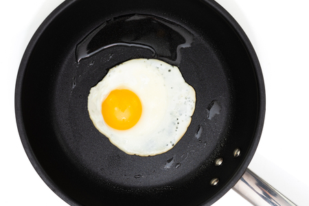 Top view of a sunny side up fried egg on a black pan isolated on a white background.の写真素材