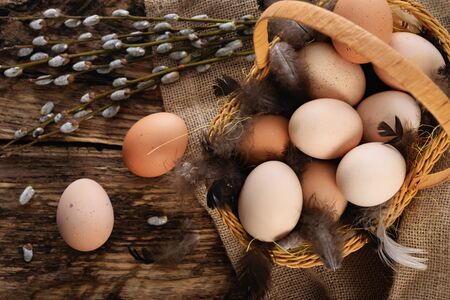 Easter composition in vintage style - wicker basket with eggs, feathers and willow cats on a burlap...