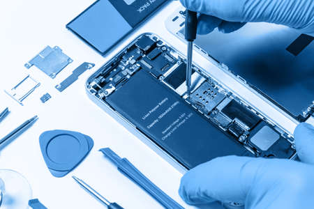 Professional occupation services concept - technician or engineer is repairing modern smartphone motherboard in the professional laboratory (blue toned)の写真素材