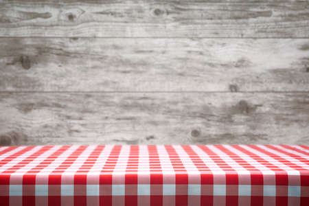 Italian cooking template - blank table with a red checked tablecloth on the blurred wooden vintage...