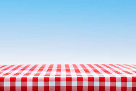 Italian cooking template - blank table with a red checked tablecloth on a blue sky background with copy space.の写真素材