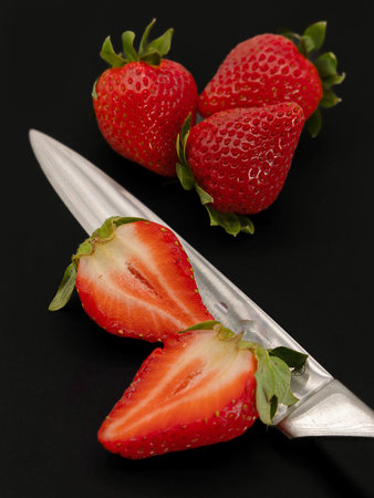 Strawberries on a black background with a knife in the foregroundの写真素材