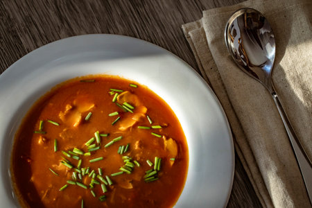 goulash soup in a white plate on a wooden table with a spoon
