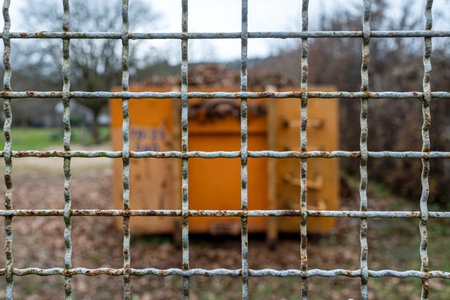 Rusty metal mesh fence with a yellow trash can in the background
