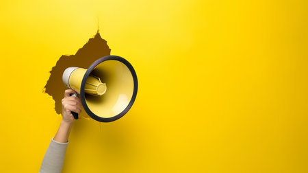 small size Hand holds a megaphone on a pastel yellow backgroundの素材