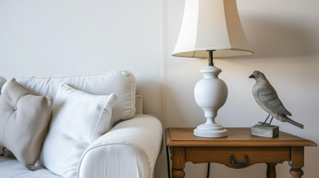 Lamp with bird statue decor on wooden night stand by white couch in living room at studio apartmentの素材