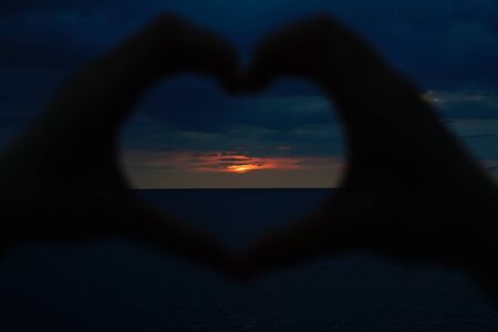 Heart shaped made of hands facing sunsetの写真素材