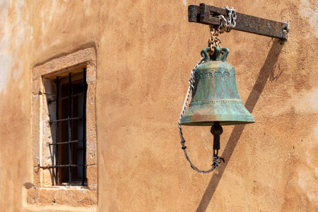 A historical bell in front of a Mediterranean wall