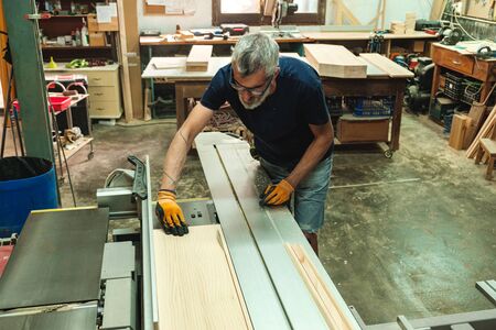 Carpenter cutting a piece of wood on the electric saw cutting machineの写真素材