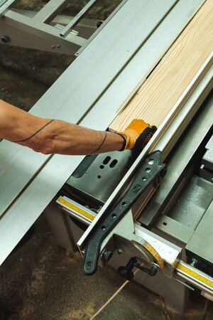 Top view of a gloved arm pushing a piece of wood into the electric saw cutting machineの写真素材