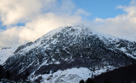 Amid a dramatic sky, a majestic mountain rises in Vall de BoÃ­, Pyrenees. Snow blankets its...