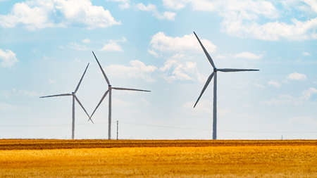 Three wind turbines sit in crop field on hot day with heat hazeの写真素材