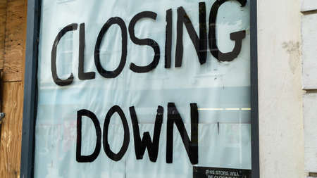 Closing down sign in a boarded-up shop windowの写真素材