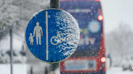Blue shared footpath sign in falling snow with public transport bus in the backgroundの写真素材