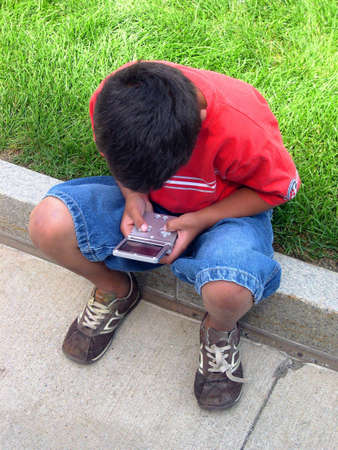 Boy playing a video game outdoors. This was an easy shot to get since this is all the boy does. He's still in that same spot right now.の写真素材