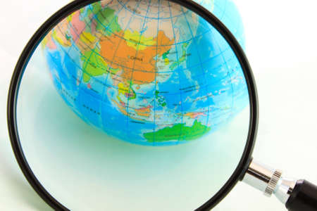 A magnifying glass view of a small colored globe isolated on a white backgroundの写真素材