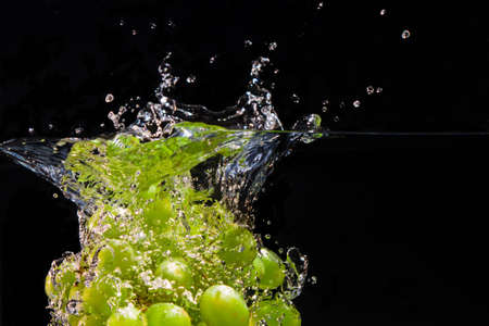 A bunch of grapes dropped into water creates sparkling splashes of dropletsの写真素材