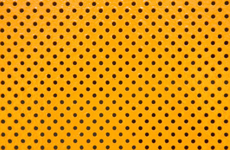 An orange metal sheets full of holes serving as a rough looking backgroundの写真素材