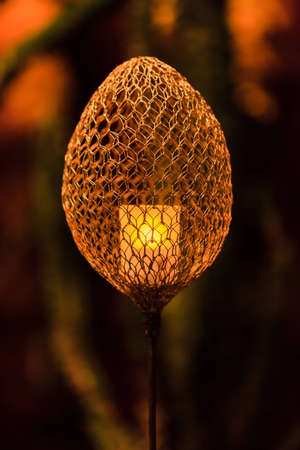 A wire mesh tea light torch subtely illuminates a gardenの写真素材