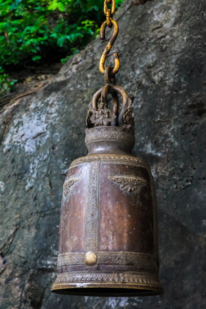 An ancient ornate temple bell hanging on a golden chain by a cliffの写真素材