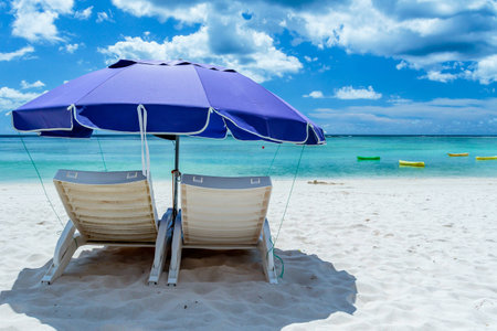 A pair of beach chairs under an umbrella on a deserted beach with white sand.の写真素材