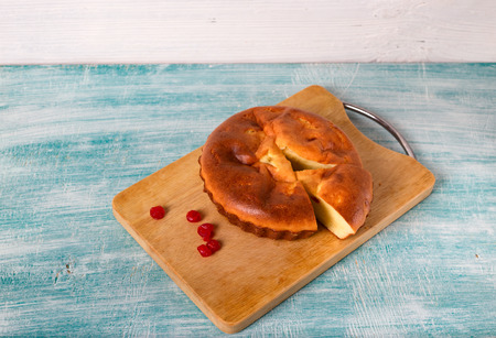 Home-made pie and several red berries nearby. Pie lies on a wooden board, a blue table in rural...